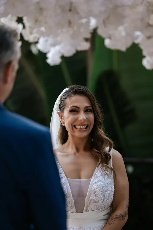 Noiva sorrindo emocionada diante do noivo na cerimônia